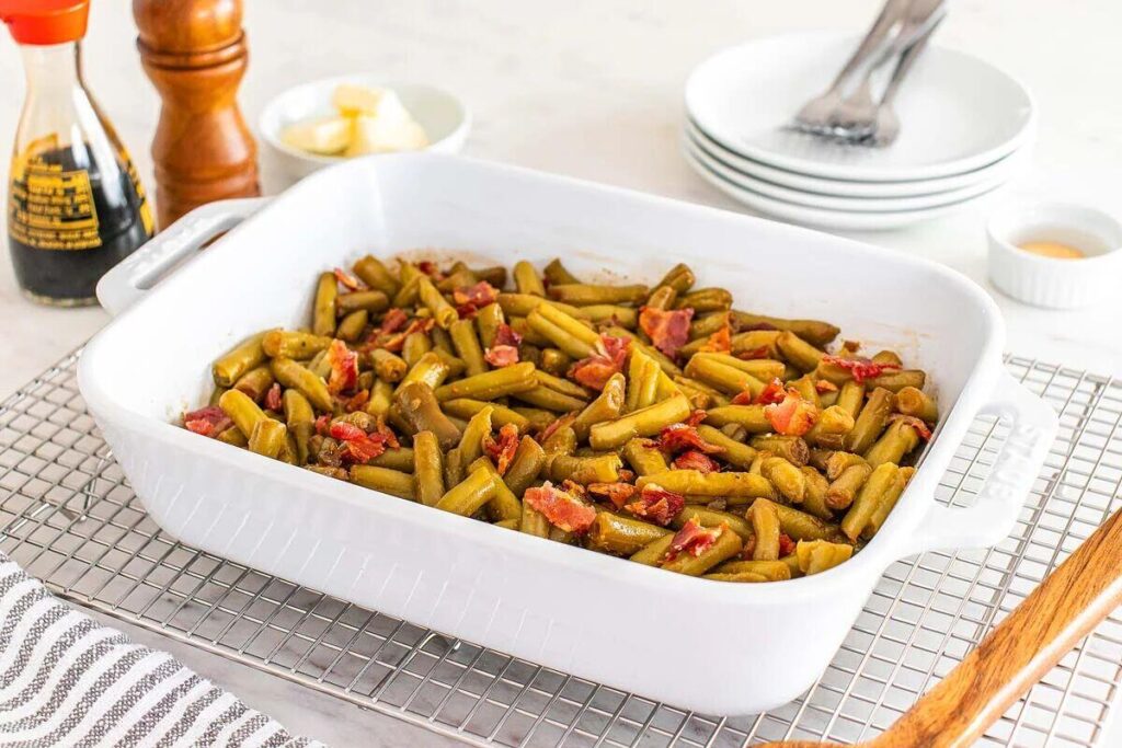 White casserole dish with cooked green beans and bacon on a cooling rack.