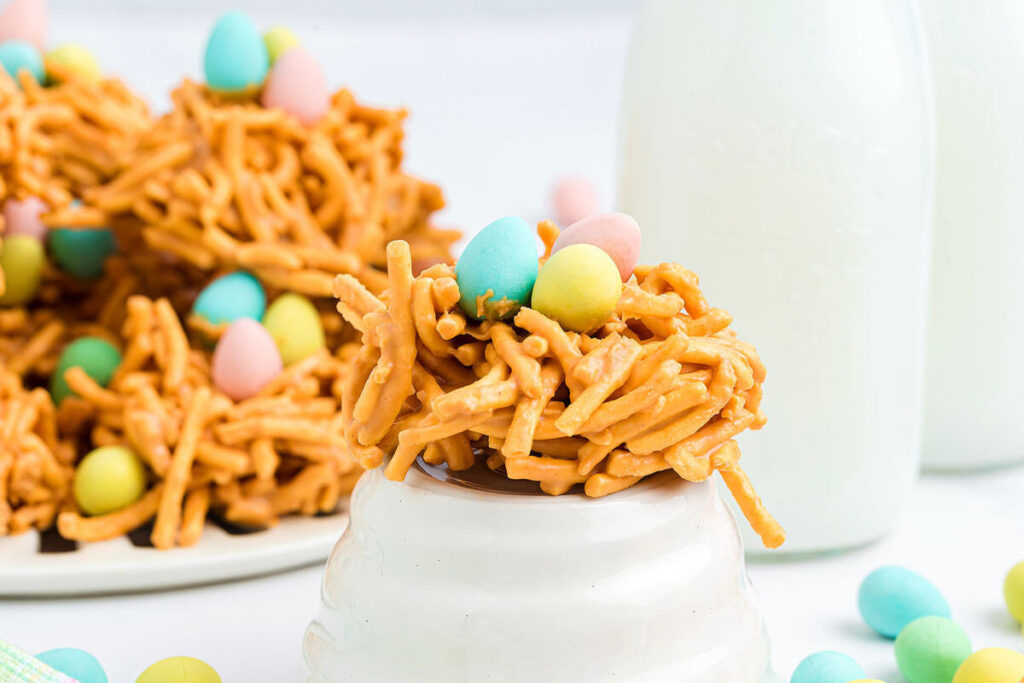 Easter haystacks are crunchy nests crafted from chow mein noodles and butterscotch, crowned with pastel-hued chocolate mini eggs, displayed beside milk bottles.