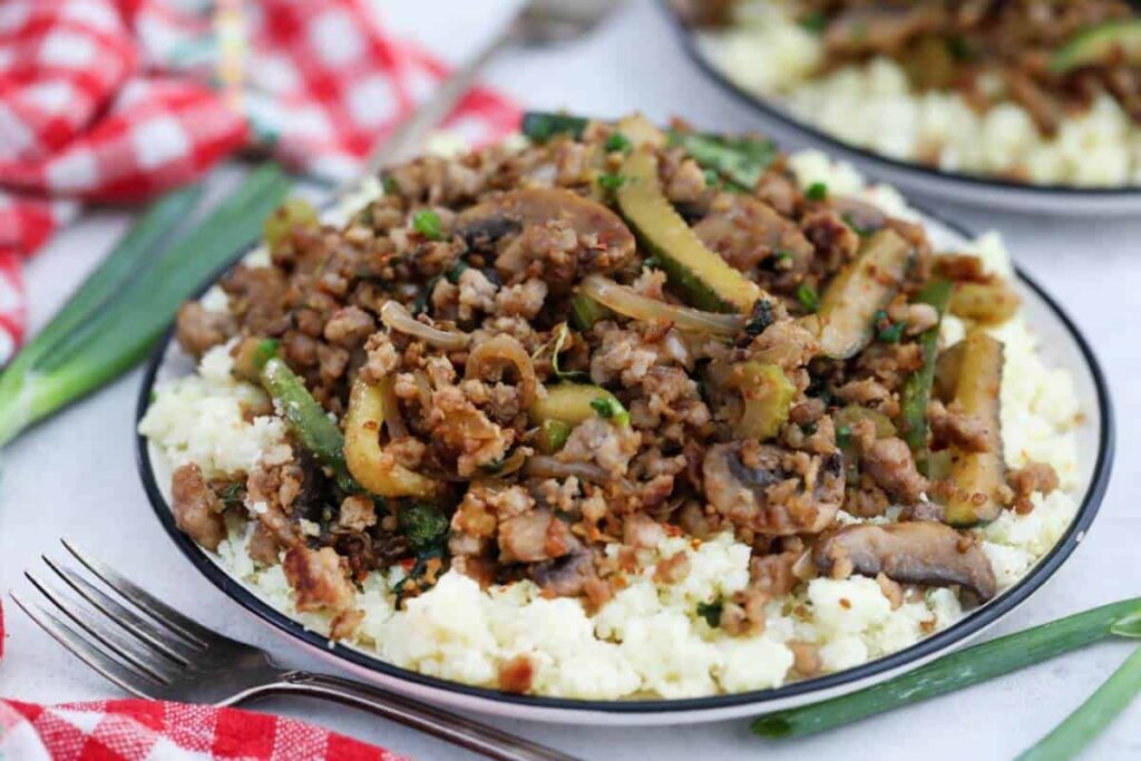 A plate with ground pork and vegetables on top of cauliflower rice.
