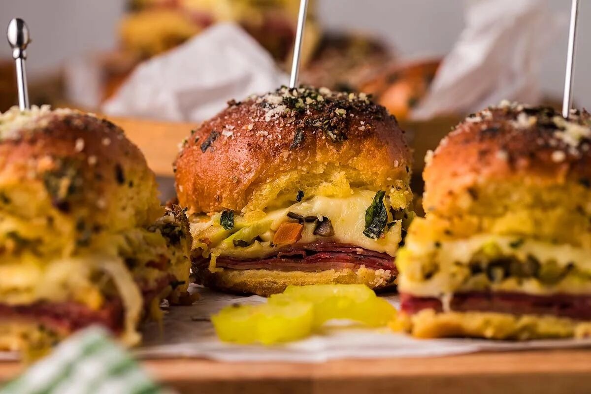 Close-up of sesame seed-topped sliders filled with sliced meat and melted cheese.