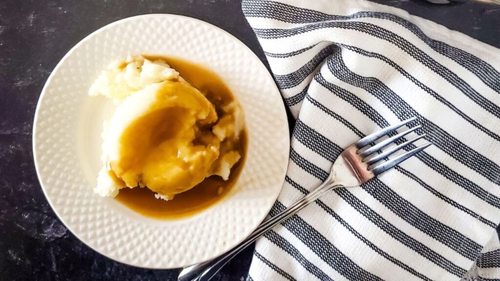 A plate of mashed potatoes smothered with Guinness Gravy on a white plate.