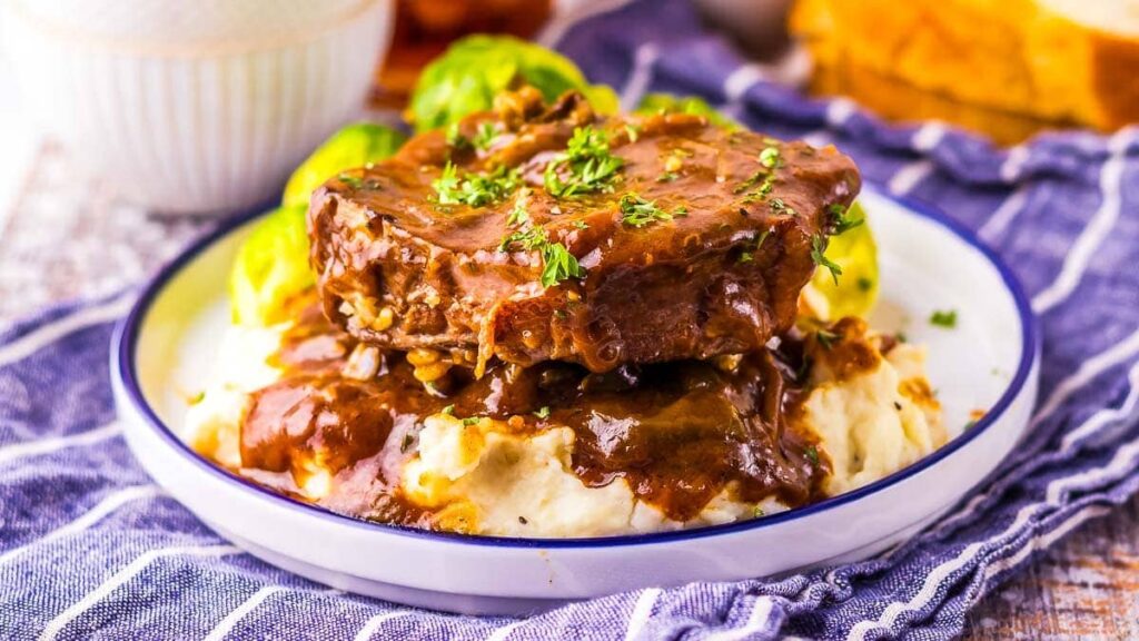Slow Cooker Smothered Steak on a bed of mashed potatoes.