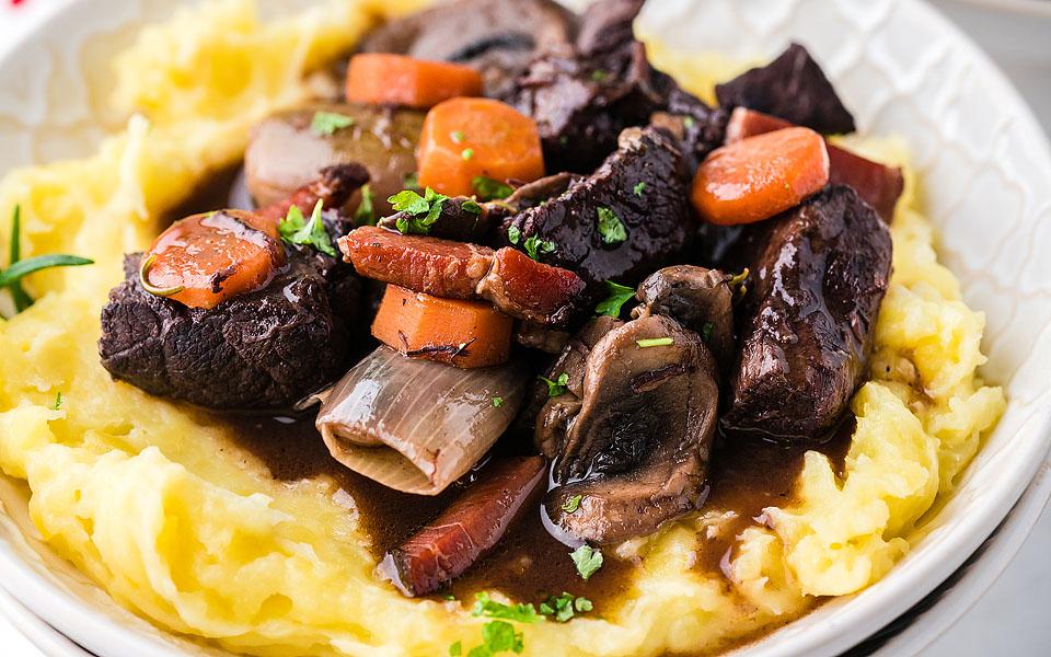 Boeuf Bourguignon over mashed potatoes in a white bowl.