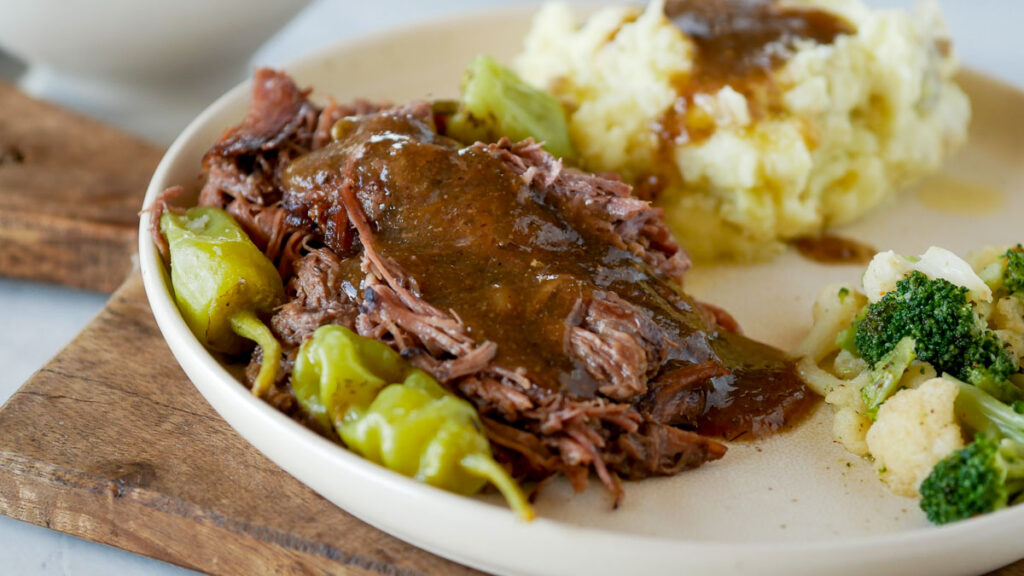 Mississippi Pot Roast on a  plate with peppers and mashed potatoes.