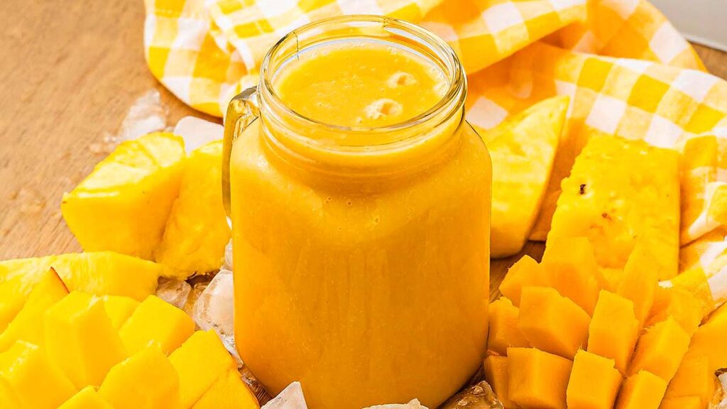 On orange colored mango smoothie surrounded by fresh chopped mango.