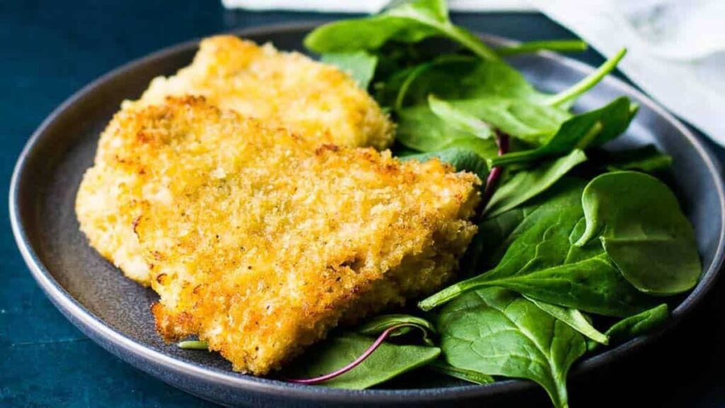 Panko Crusted Rockfish on a dark plate next to a fresh spinach salad.
