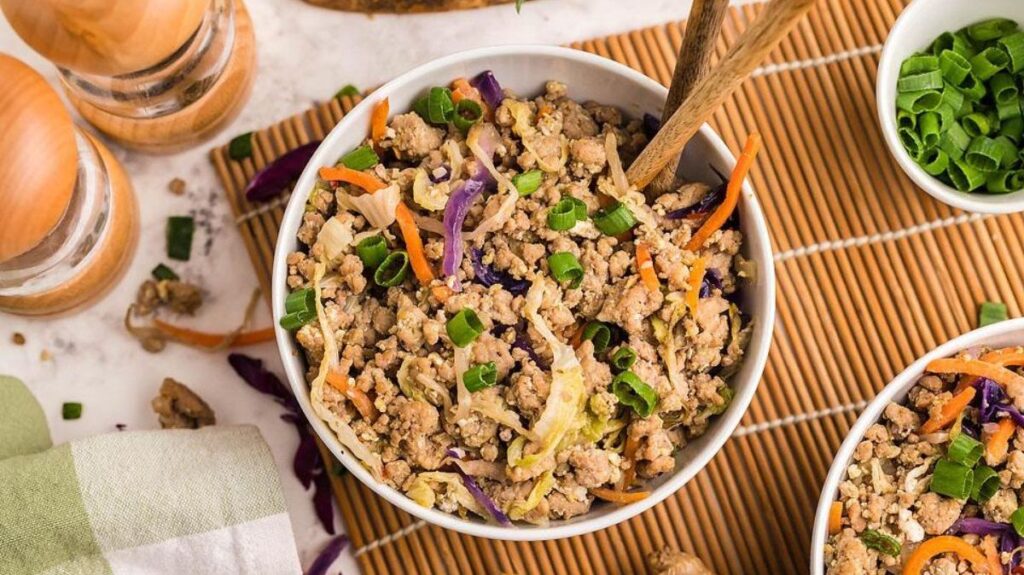 Ground pork egg roll in a bowl with cabbage, carrots, and green onions served with chopsticks.