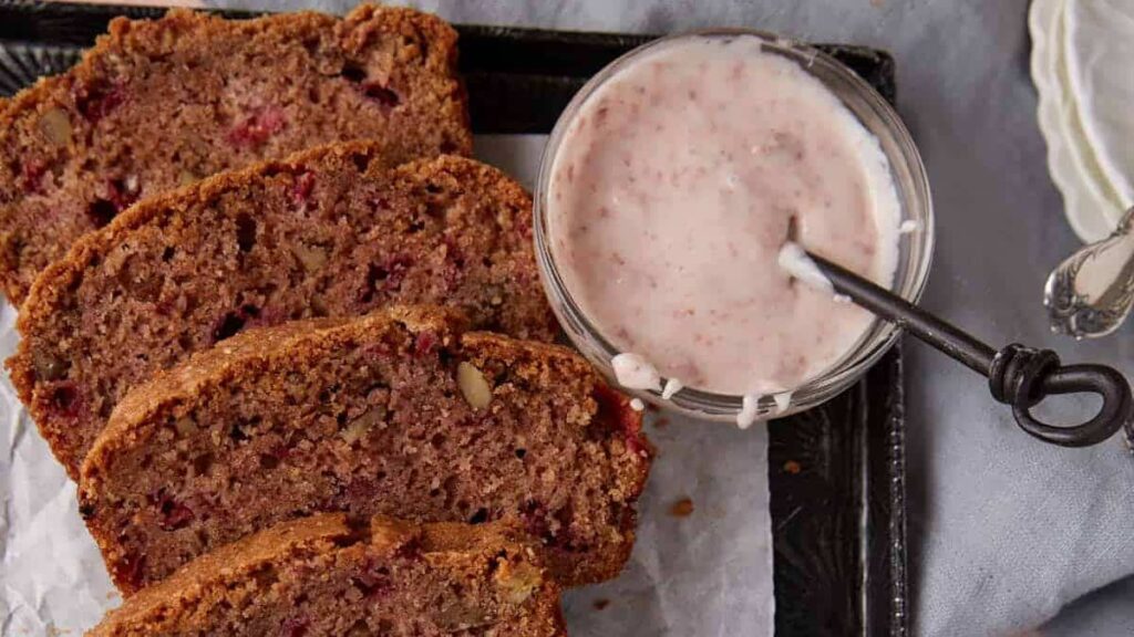A sliced loaf of Strawberry Quick Bread next to a light pink Strawberry Glaze.