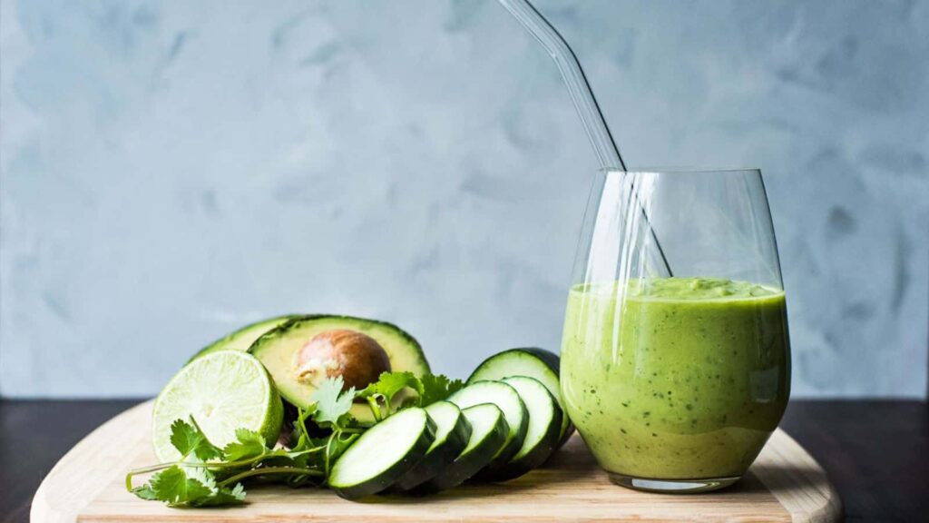 A green smoothie with cucumbers, cilantro and avocado on a wooden cutting board.