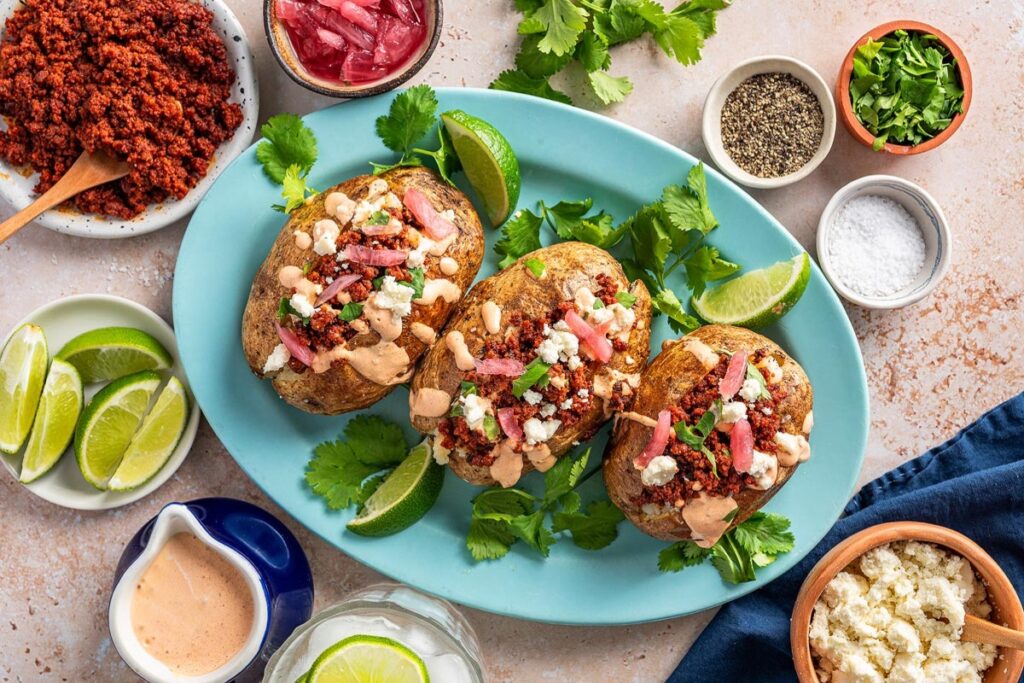 Three loaded chorizo baked potatoes rest on a blue plate, adorned with toppings like sour cream and cheese. 