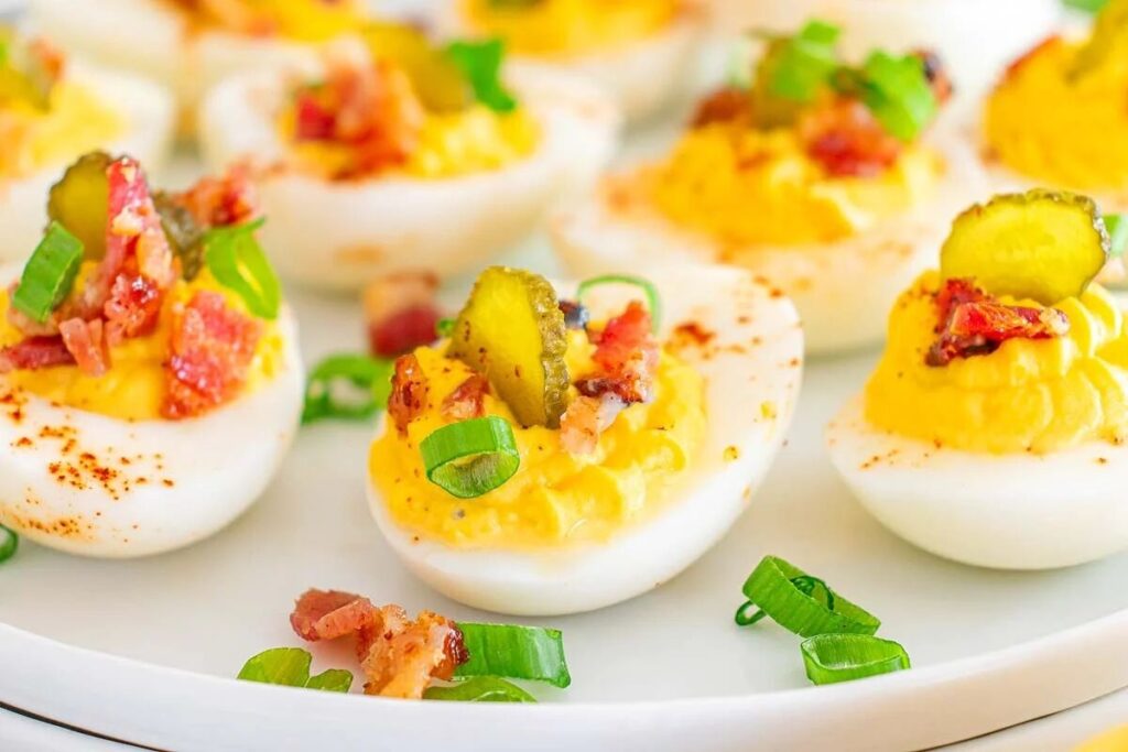 Million dollar deviled eggs topped with crispy bacon, tangy pickles, and fresh green onions make a delightful presentation on a white plate.