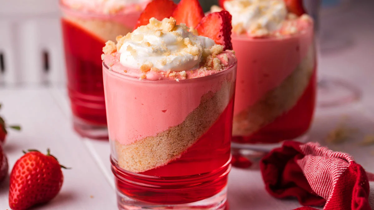 Several small tartlets filled with pink mousse and topped with sliced strawberries and dollops of cream on a rack.