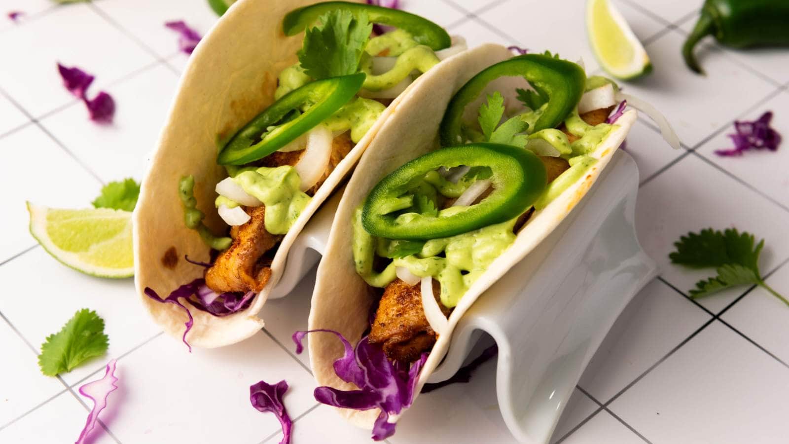 Two tilapia tacos with grilled fish, sliced jalapeños, cilantro, onions and other ingredients.
