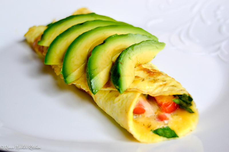 A veggie omelet on a white plate topped with fresh avocado.