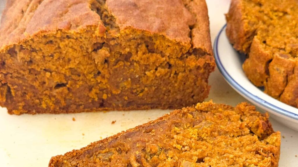 Moist and healthy pumpkin banana bread with golden raisins on a white cutting board.