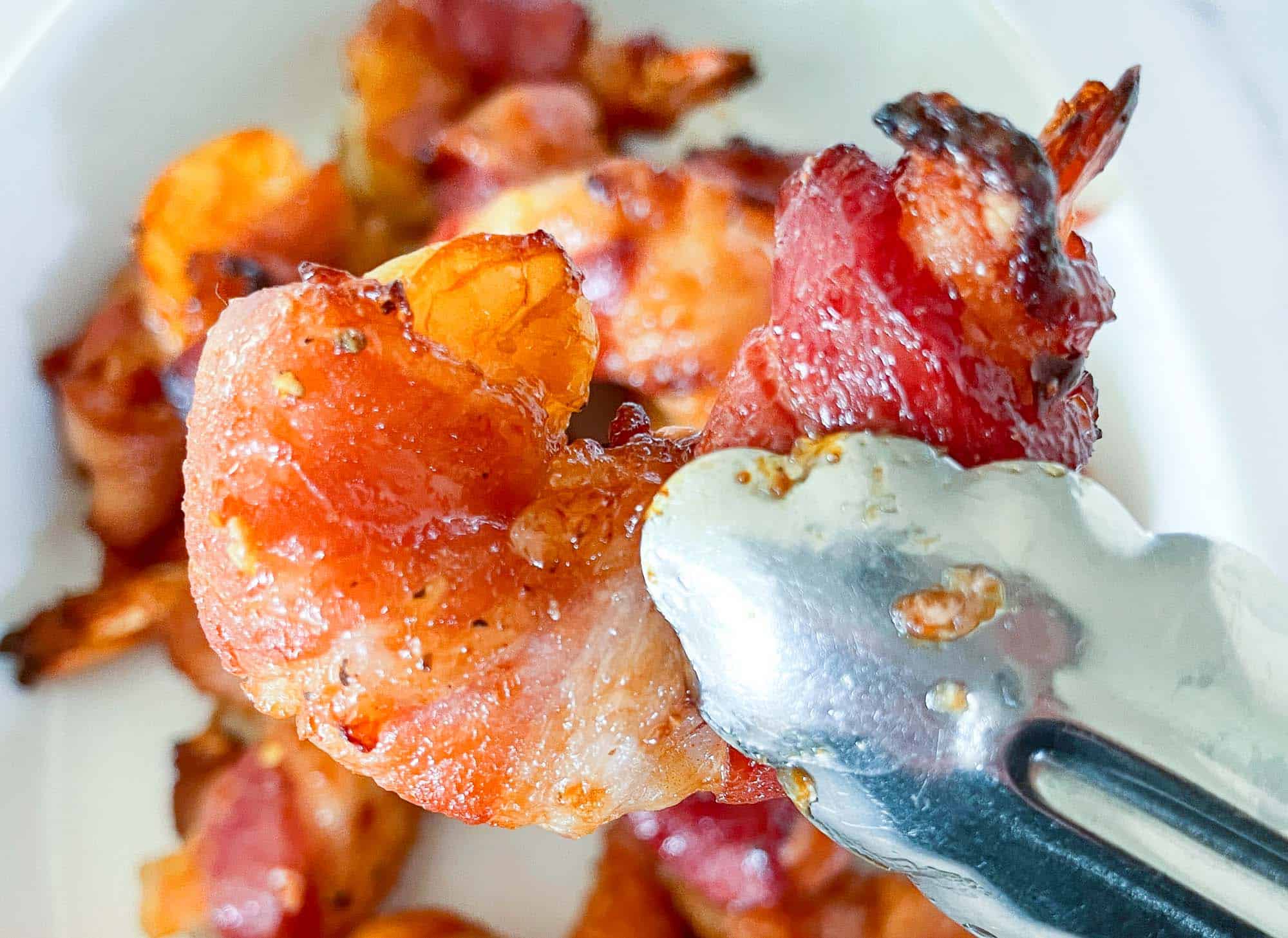 A bacon wrapped shrimp being held up over the platter of shrimp.