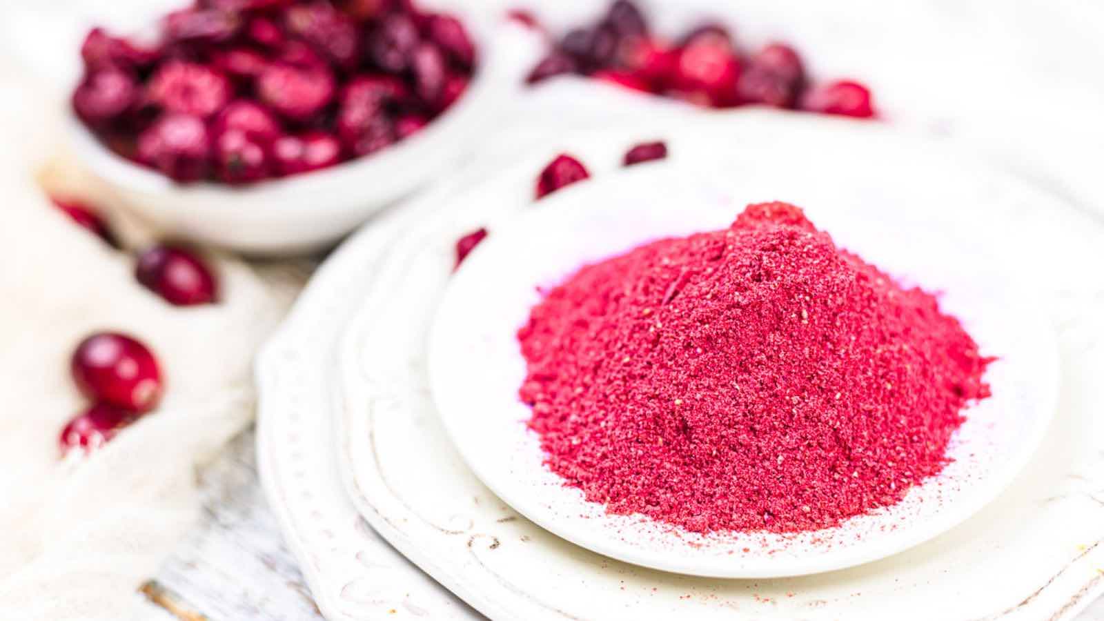 Cranberry powder on a white plate next to cranberries.