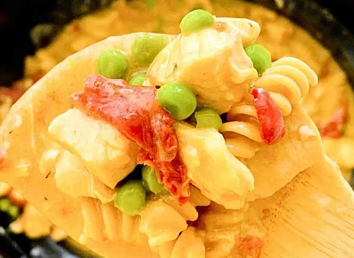 white bowl with chicken pasta with sundried tomatoes and peas and garlic and a light linen around the bowl.