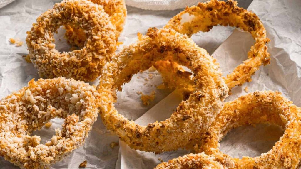 Crispy onion rings stacked on a plate with a small bowl of dipping sauce beside them.