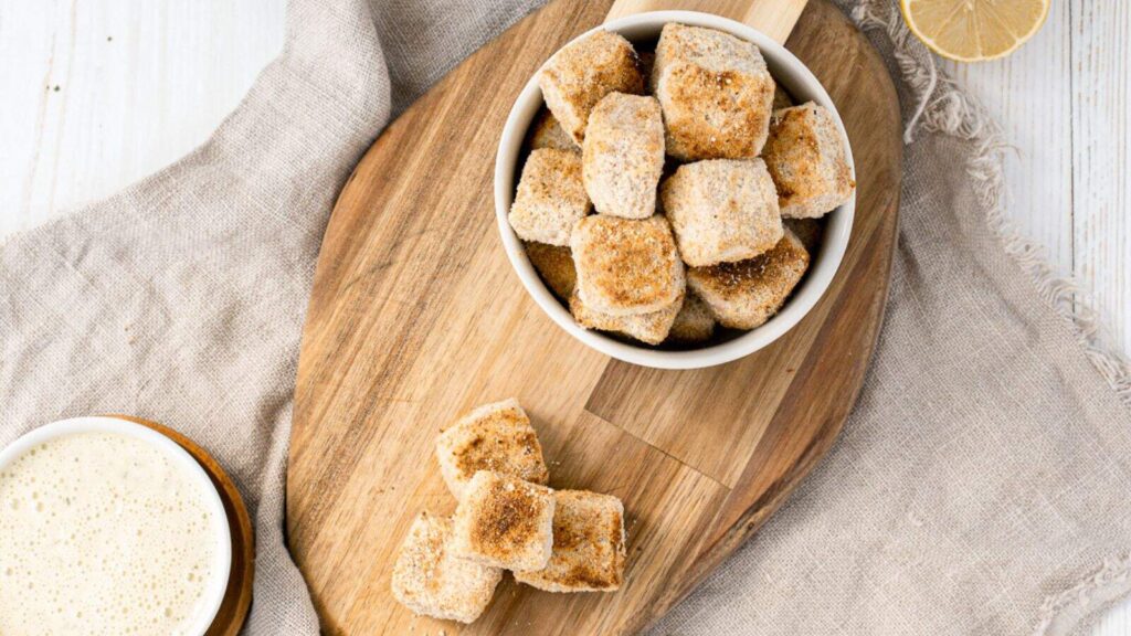 Breaded tofu bites arranged in a bowl with a small dish of dipping sauce beside them.