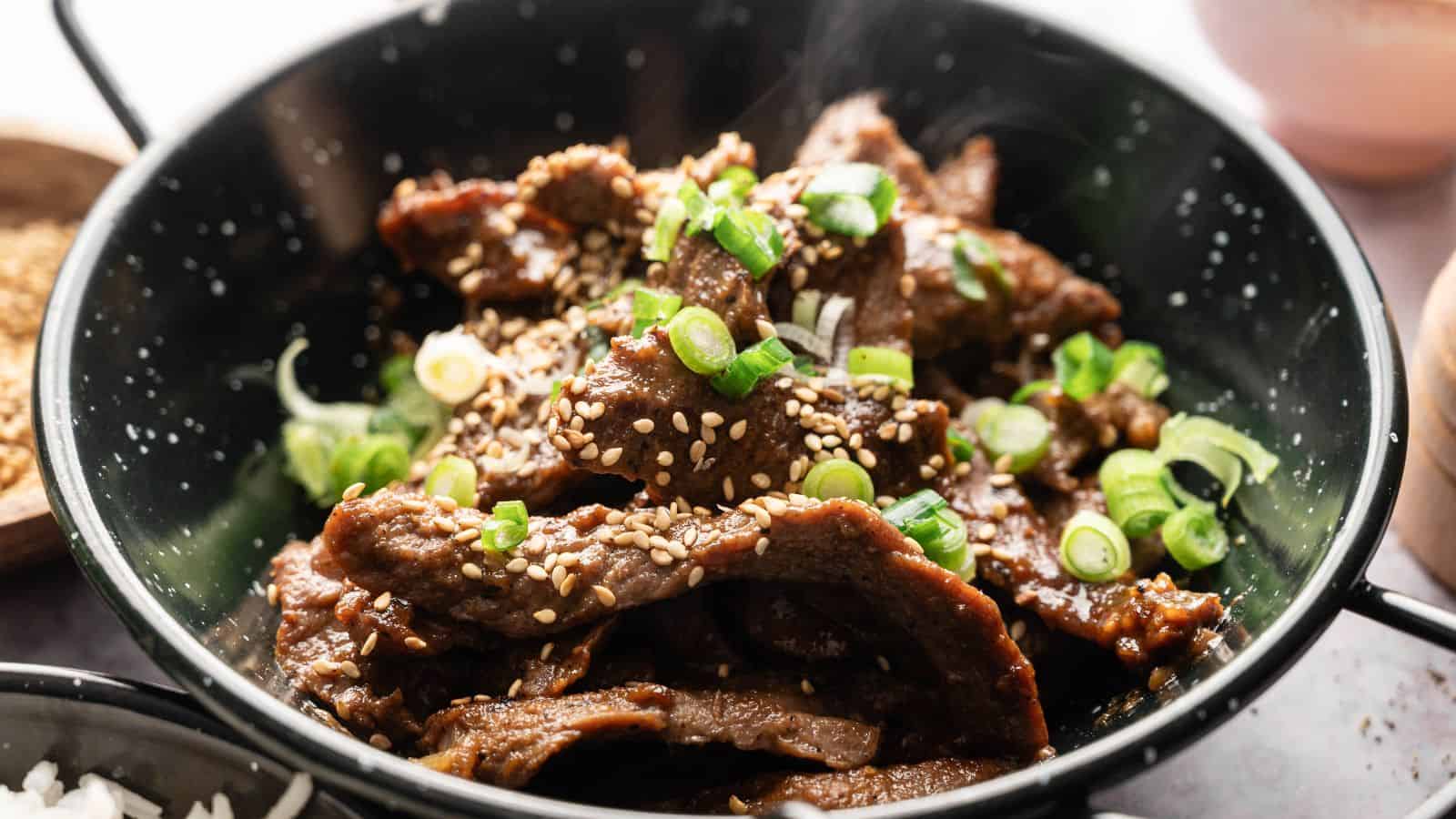 A bowl of cooked beef slices topped with sesame seeds and chopped green onions.