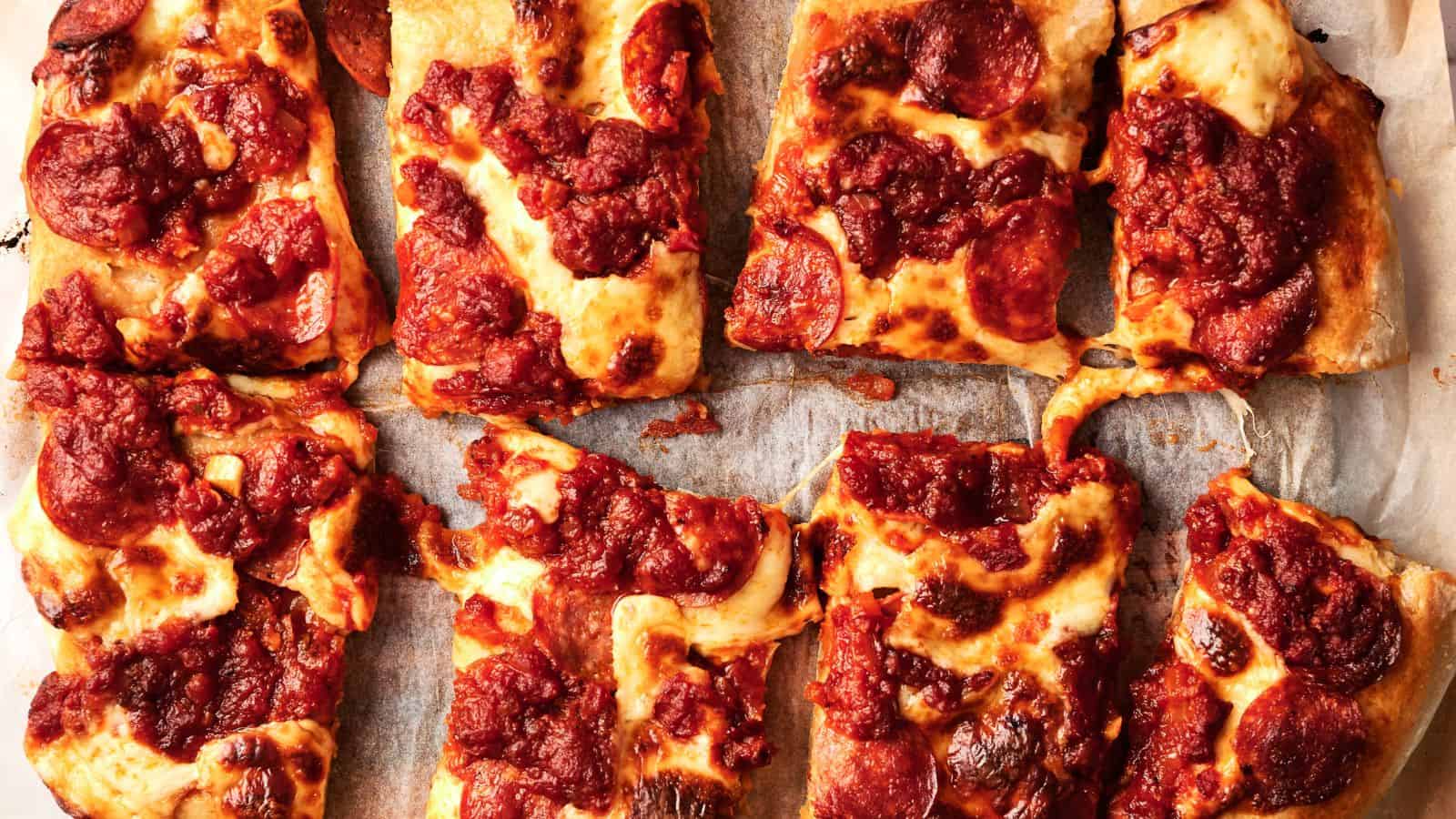 Eight rectangular slices of pepperoni pizza with thick tomato sauce and melted cheese on parchment paper.