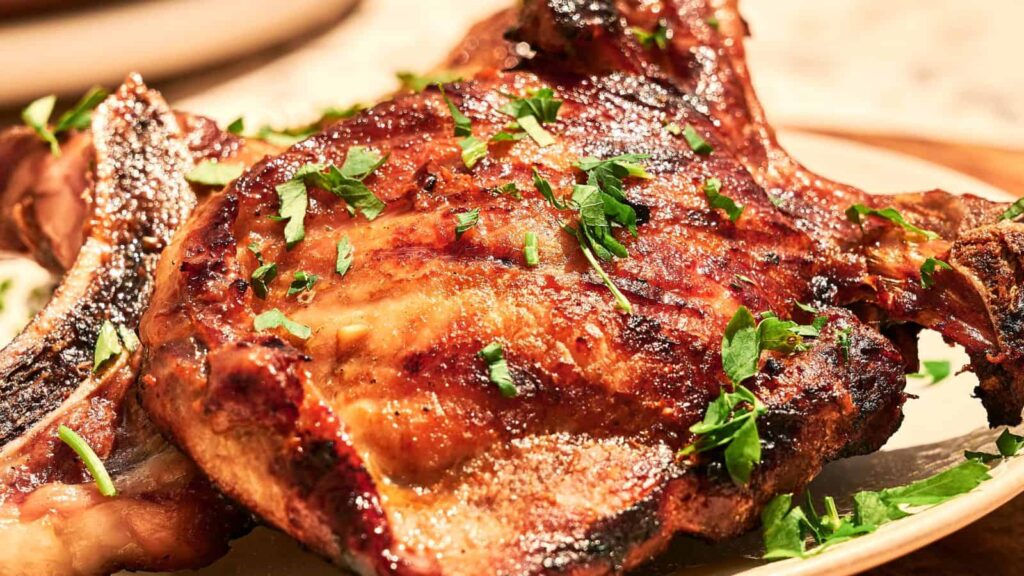 A grilled pork chop garnished with chopped parsley is served on a plate.