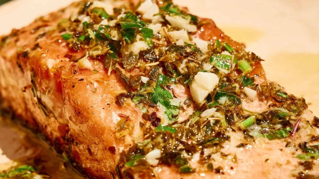 A close-up of a cooked salmon fillet topped with a mixture of chopped herbs, garlic, and seasonings.