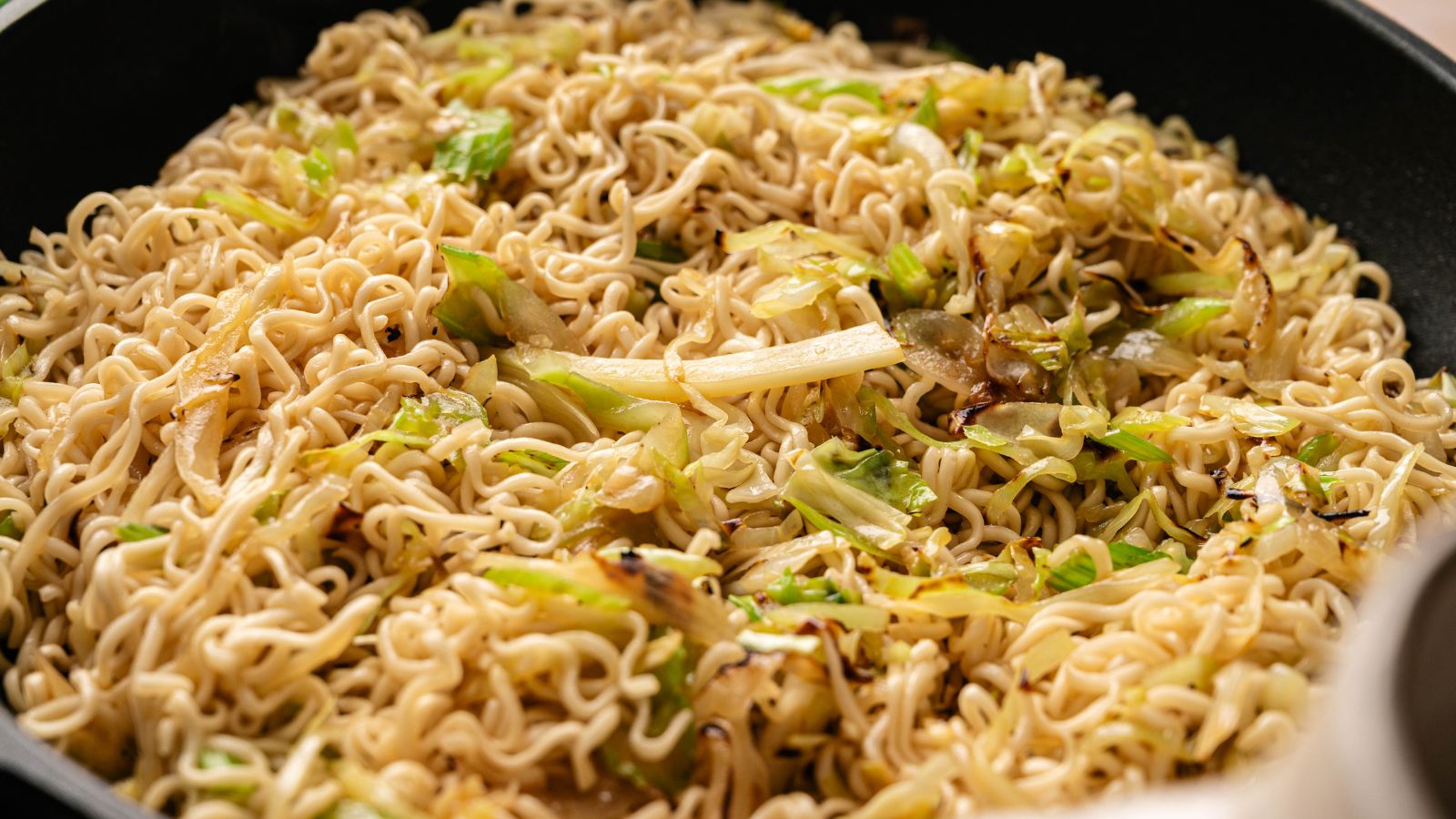 A close-up of cooked instant noodles mixed with sautéed cabbage and onions in a pan.