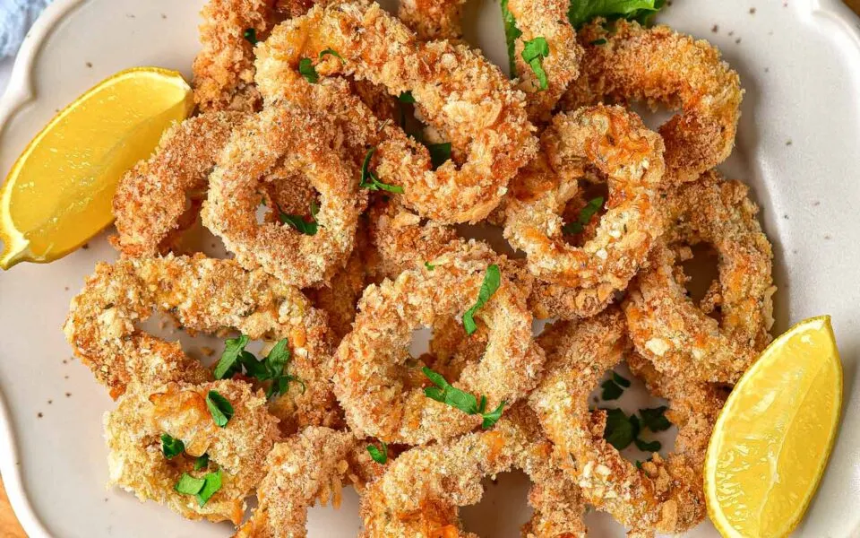 Air-fried calamari rings garnished with parsley and lemon wedges on a white plate.