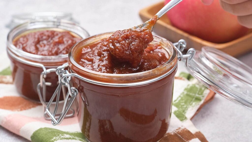 Close-up of a spoon lifting apple butter from an open jar, with another jar in the background.