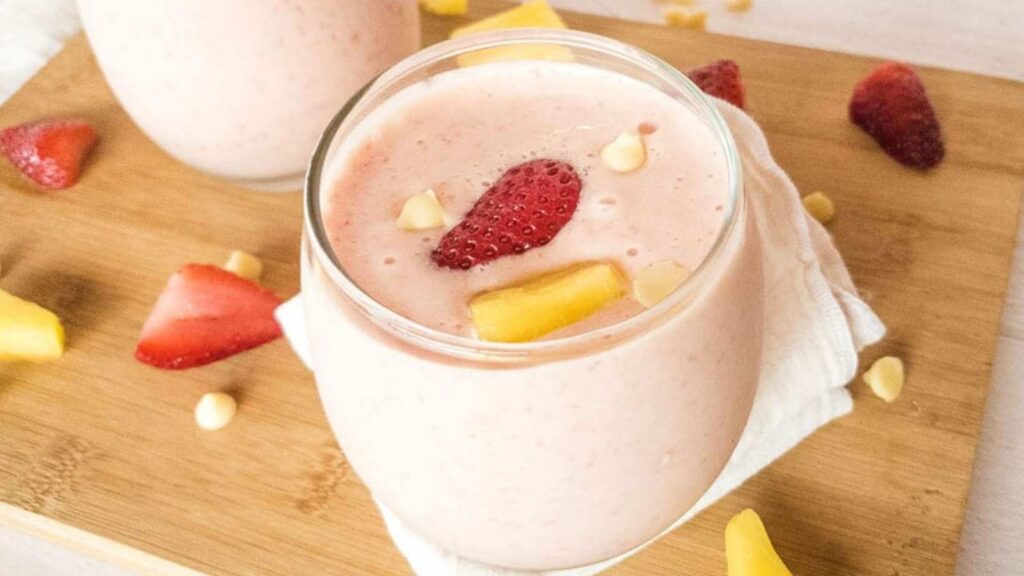 A glass of strawberry smoothie topped with sliced strawberries, yellow fruit pieces, and white chocolate chips.