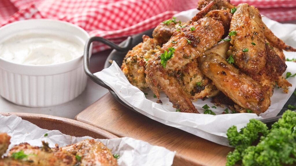 A plate of baked chicken wings garnished with parsley on parchment paper.