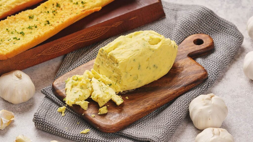 A block of garlic herb butter partially sliced on a wooden board.
