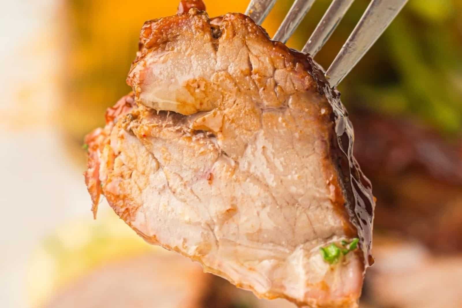 A close-up of a fork holding a juicy, cooked piece of meat with a browned exterior and tender interior.