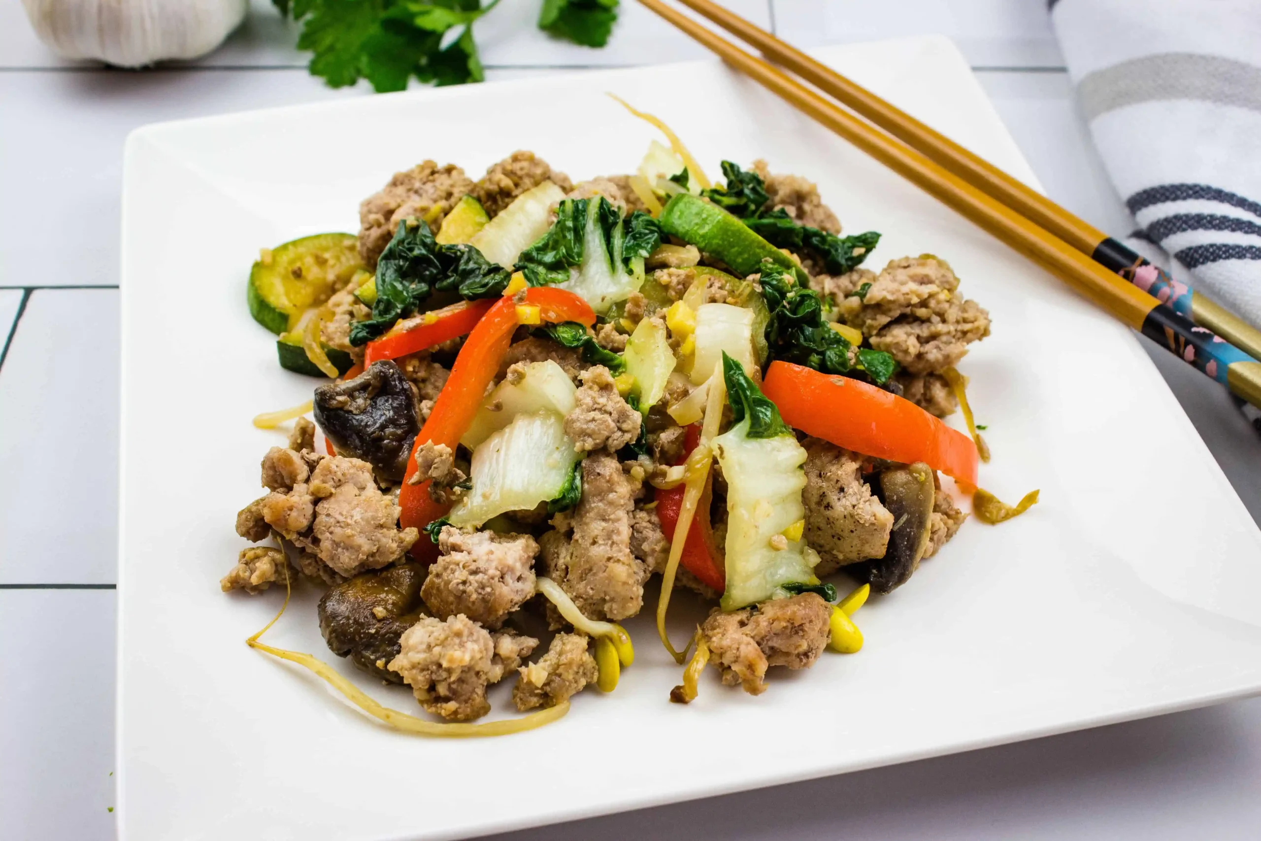 A white plate with meat, vegetables and chopsticks.
