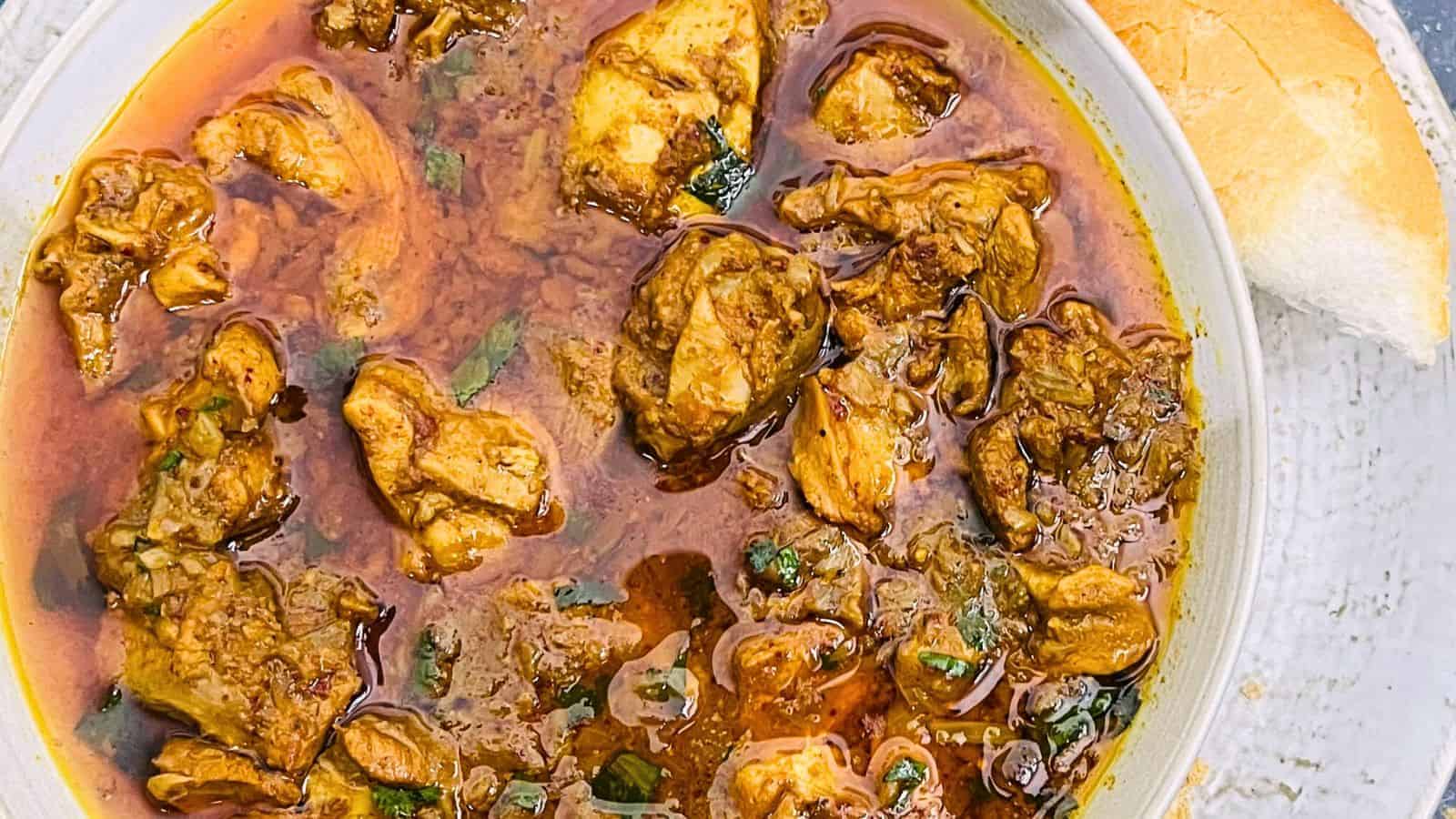 Top view of a bowl of Chicken Vindaloo garnished with herbs, accompanied by a slice of bread on the side.