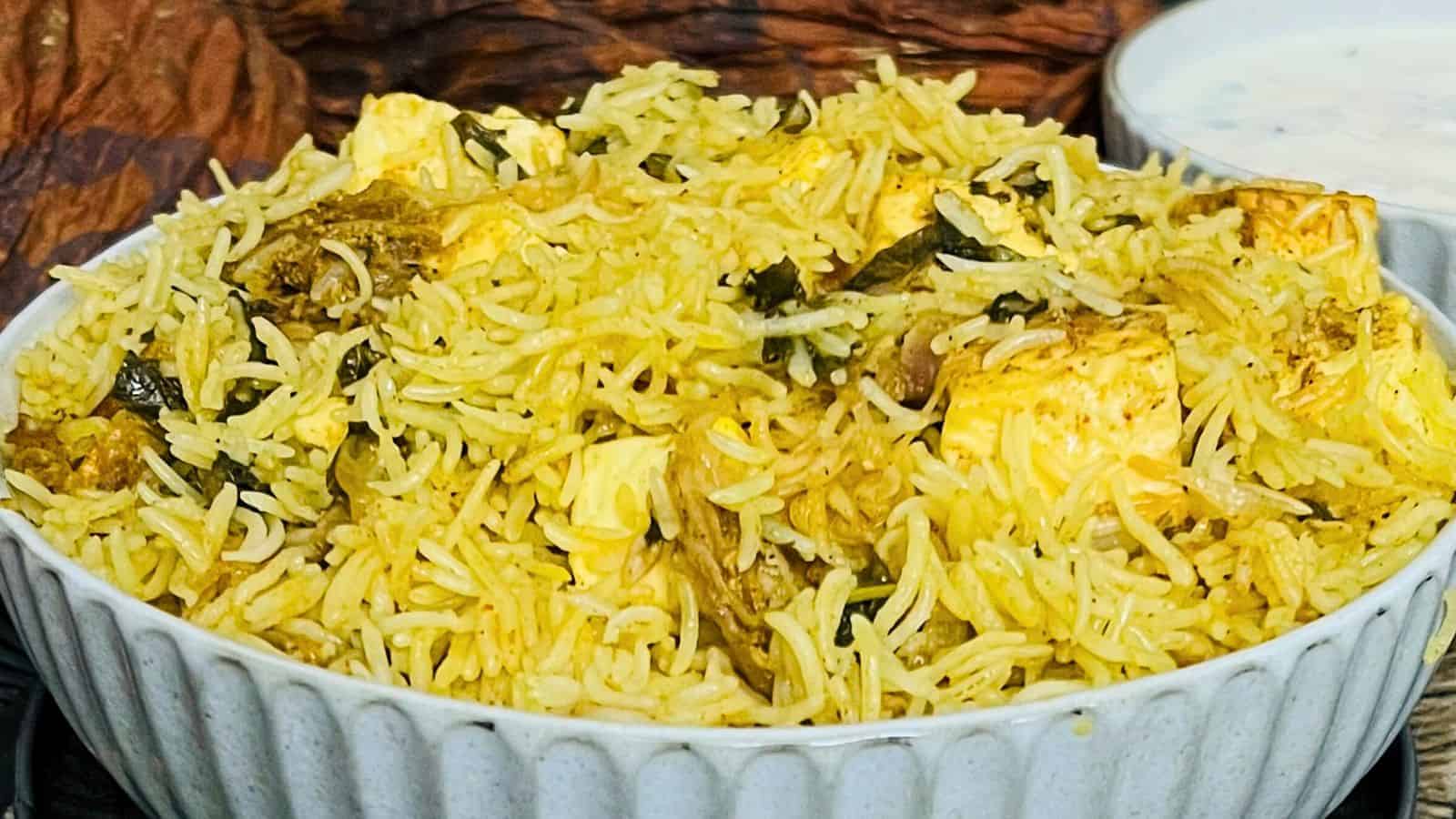 Bowl of Instant Pot Paneer Biryani with chunks of chicken, rice, and spices, served with a side of yogurt sauce.
