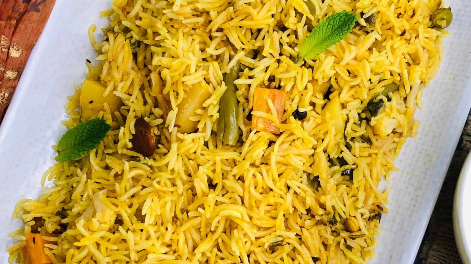 Plate of Instant Pot Vegetable Biryani, with spices, nuts, and mint leaves.