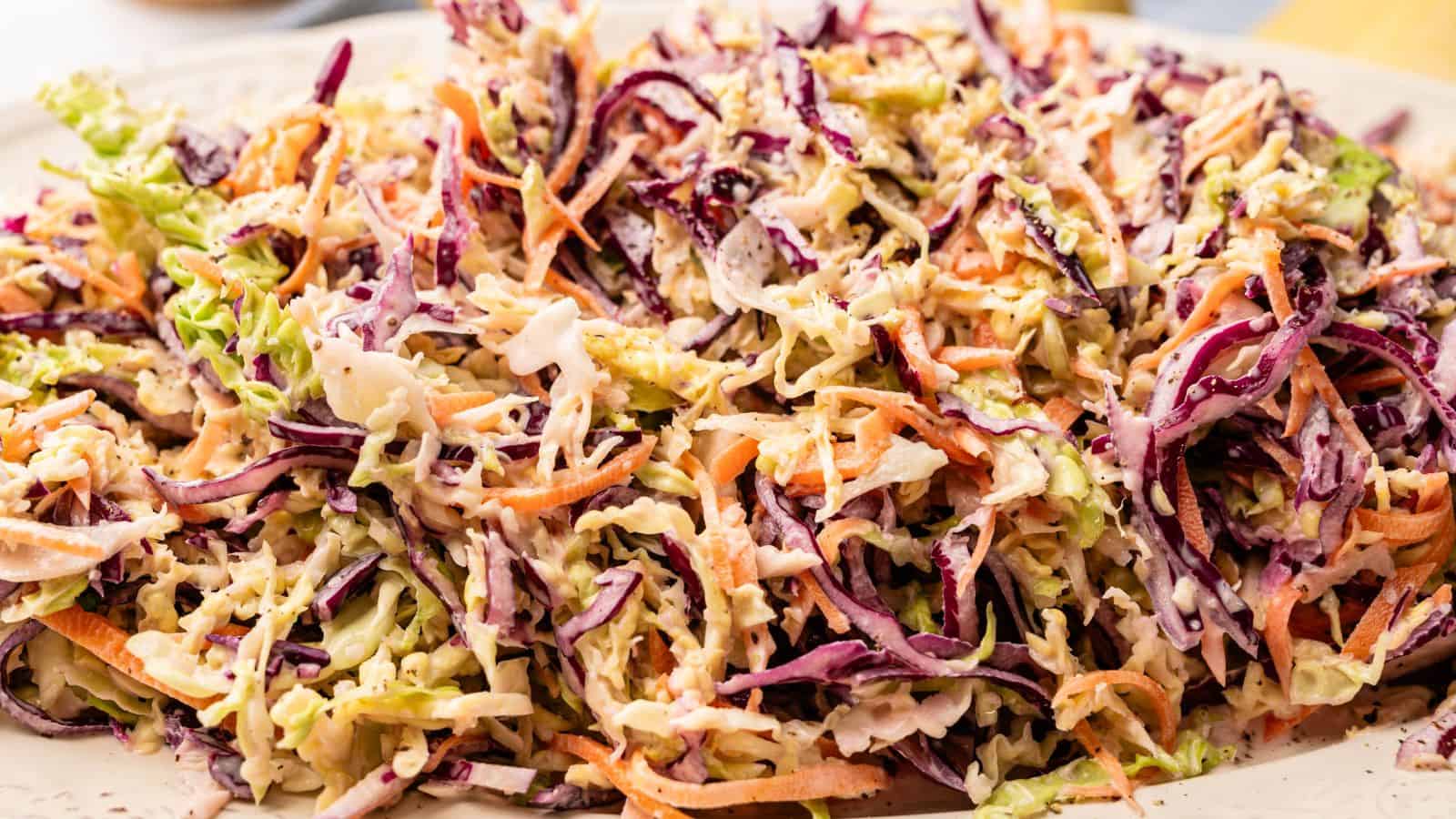 A close-up of coleslaw made with shredded green and purple cabbage, carrots, and creamy dressing on a white plate.