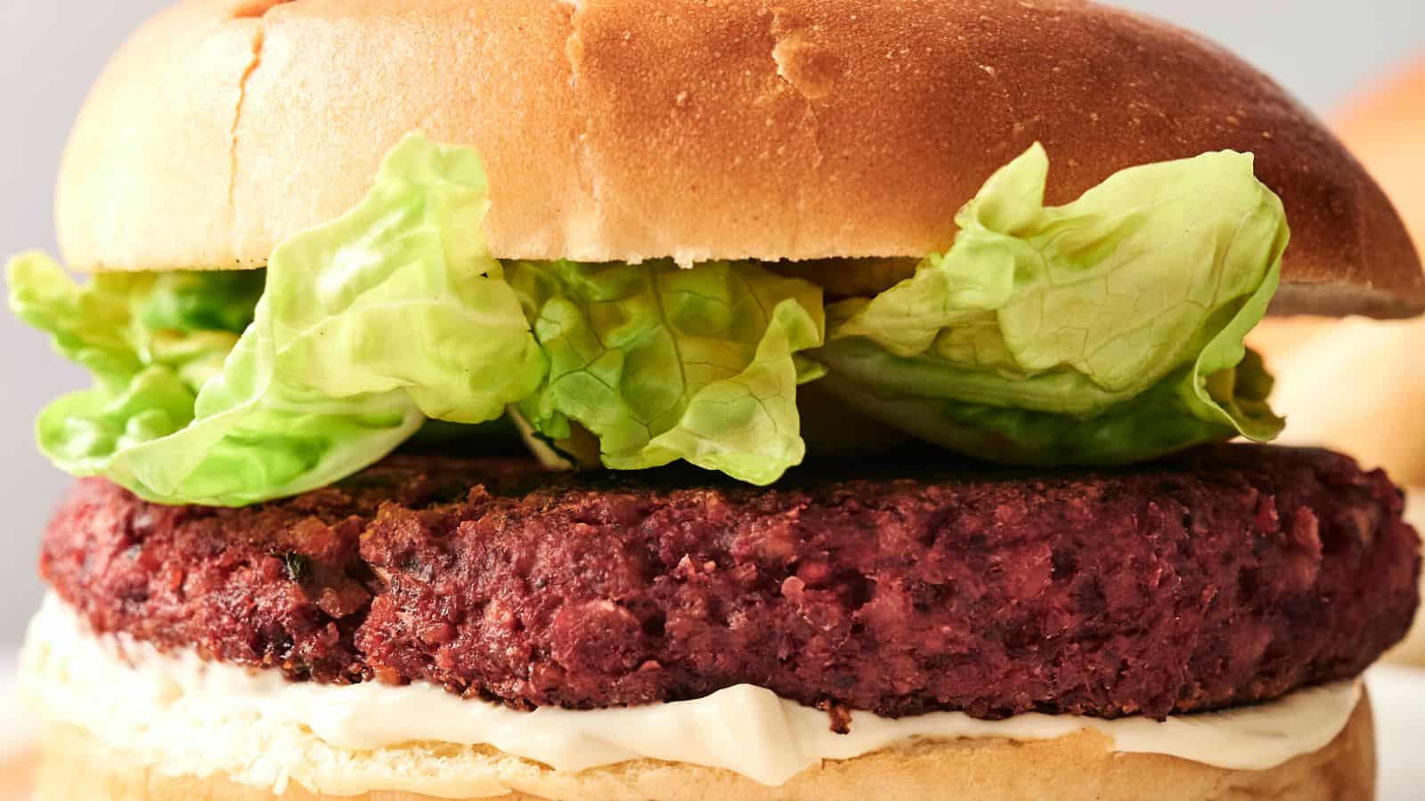 Close-up of a burger with a plant-based patty, lettuce, and sauce in a bun.