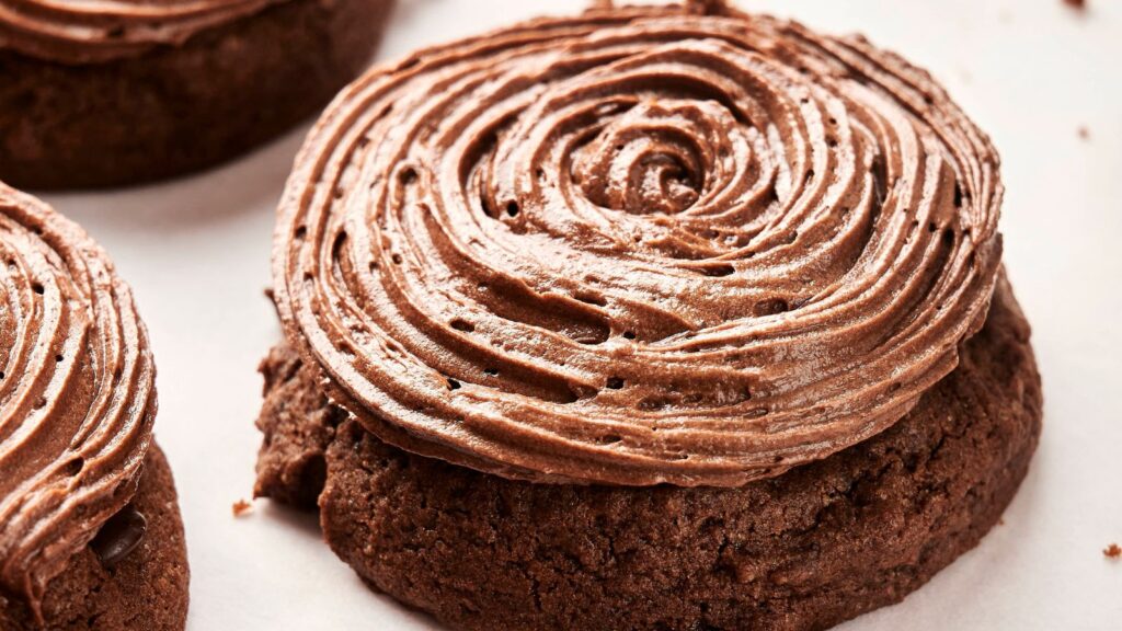 A delectable close-up of a Copycat Crumbl Chocolate Cake Cookie, crowned with a swirl of rich chocolate frosting, resting on a pristine white surface.