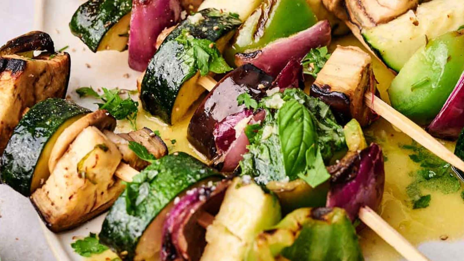 Close-up of grilled veggie kabobs with zucchini, bell peppers, eggplant, and onions, garnished with fresh herbs.