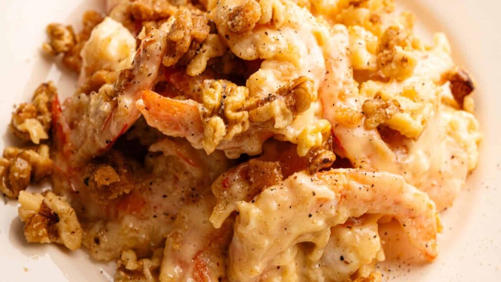 Shrimp coated in a creamy sauce, topped with chopped walnuts, served on a white plate.