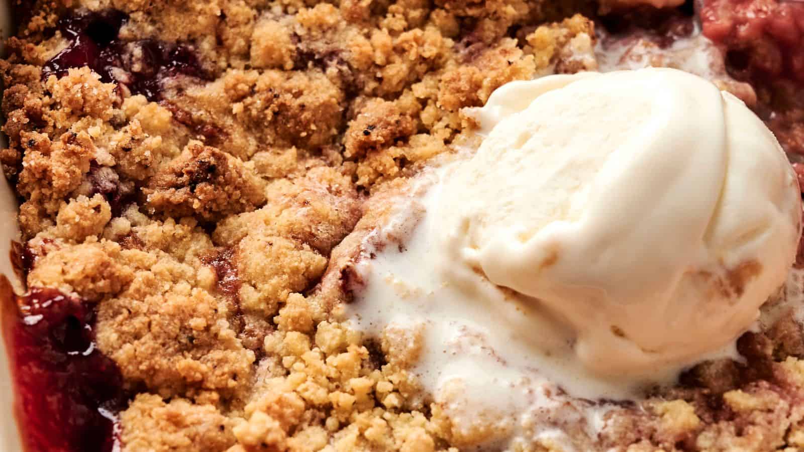 A close-up of a fruit crumble dessert topped with a scoop of vanilla ice cream.