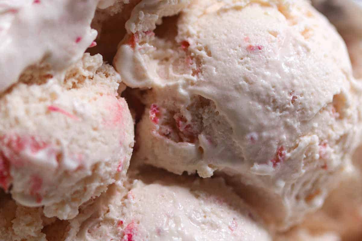 Close-up of several scoops of creamy ice cream with visible strawberry fruit pieces mixed throughout.