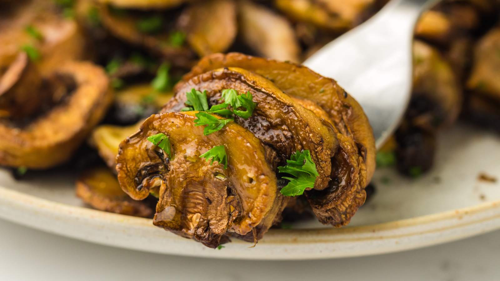 Close-up of sautéed sliced mushrooms garnished with chopped parsley on a spoon.