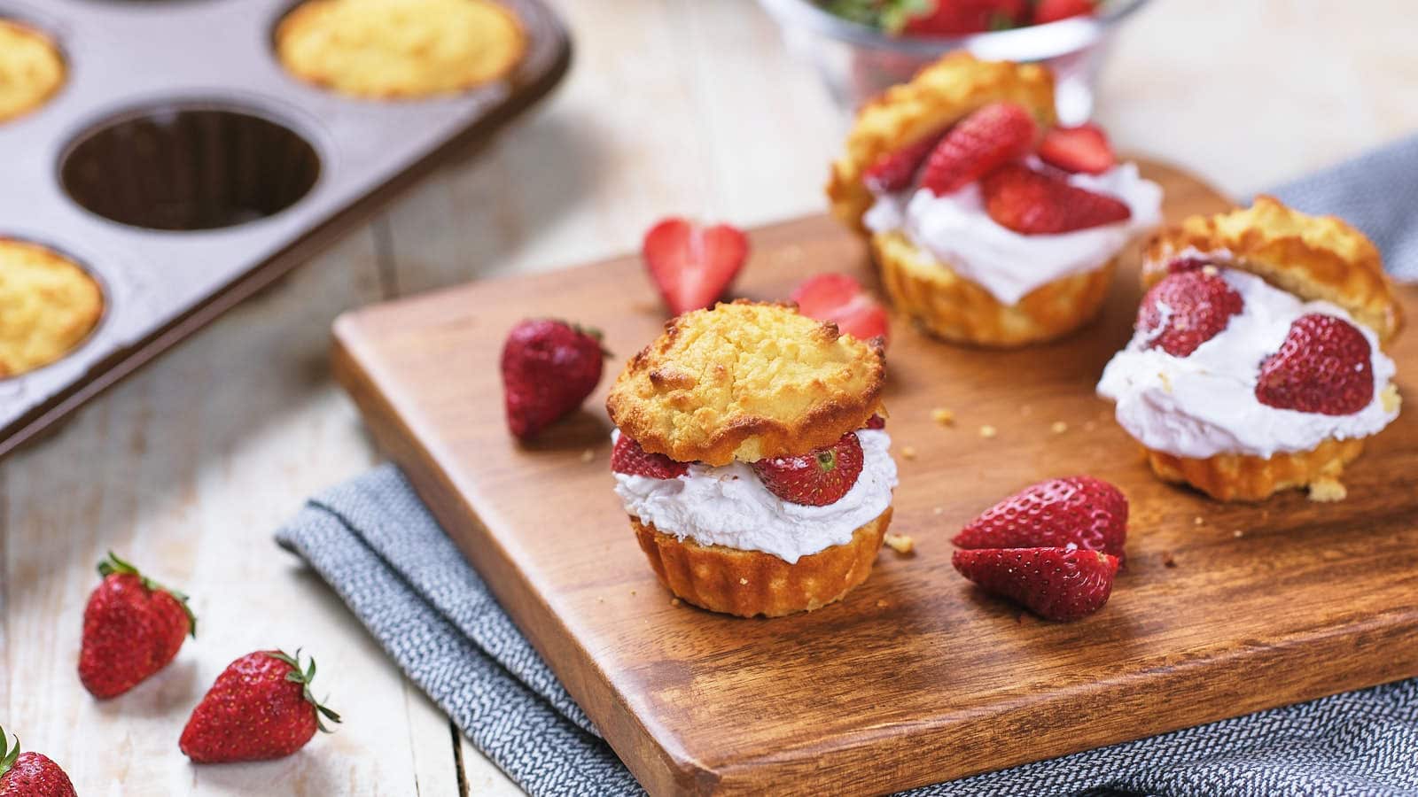 A slice of strawberry shortcake with whipped cream on a white plate, topped with a whole strawberry.