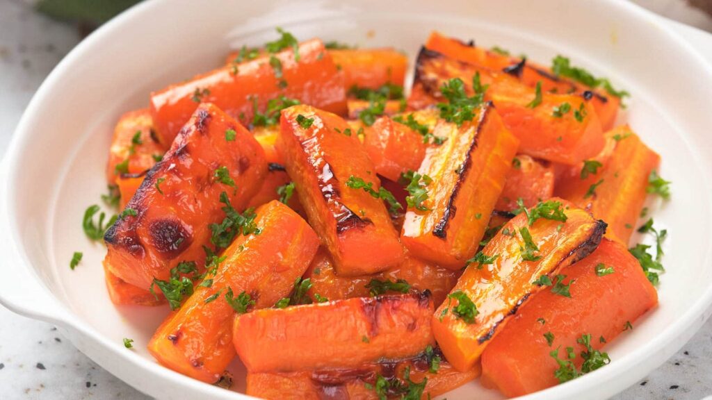 Honey roasted carrots garnished with chopped parsley in a white dish.