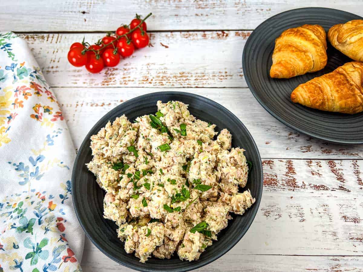 A bowl of Southern ham salad and a plate of croissants on a wooden table.